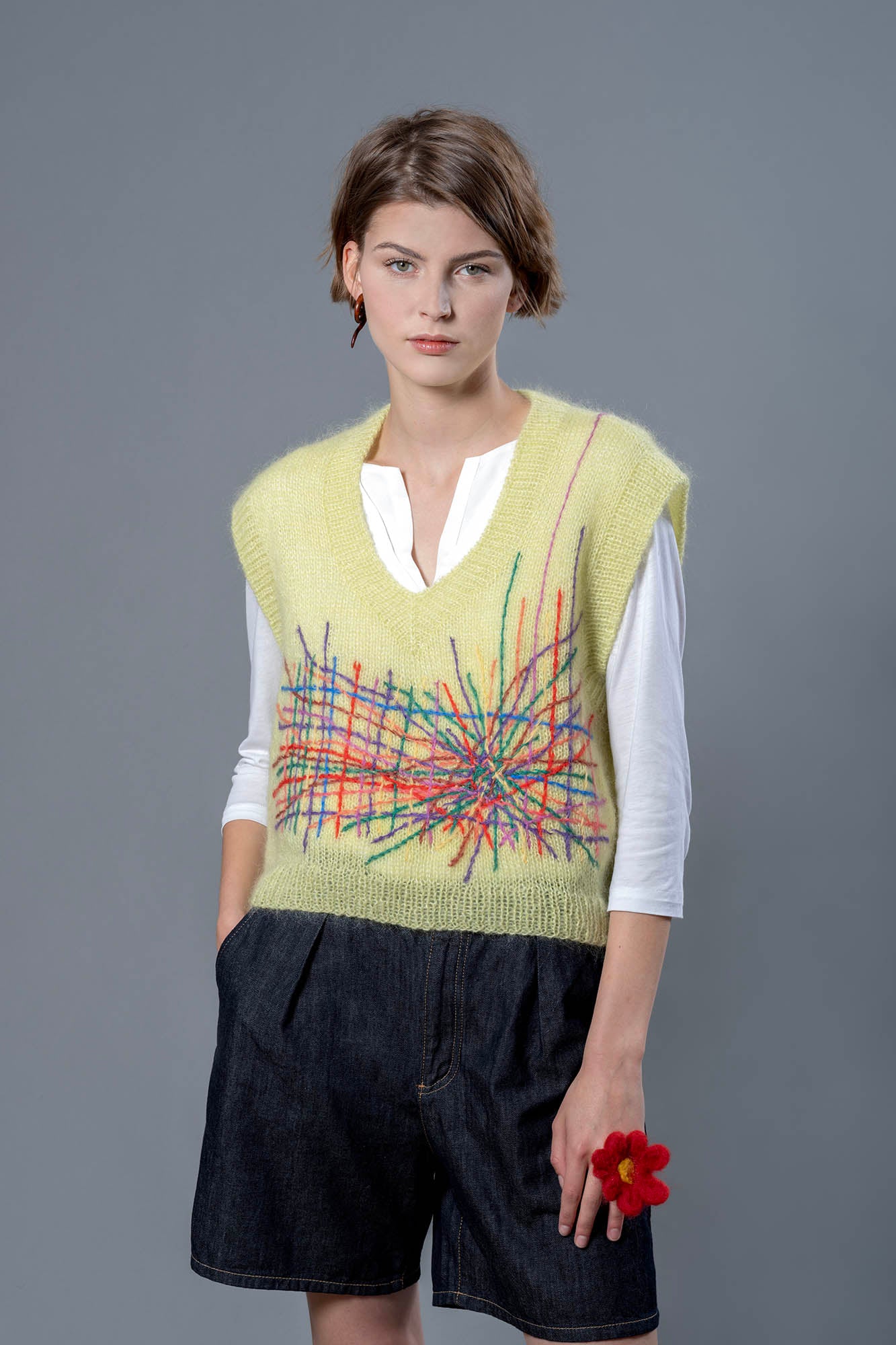 Woman wearing a yellow mohair vest. The vest has a multitude of colourful embroidered lines in its center