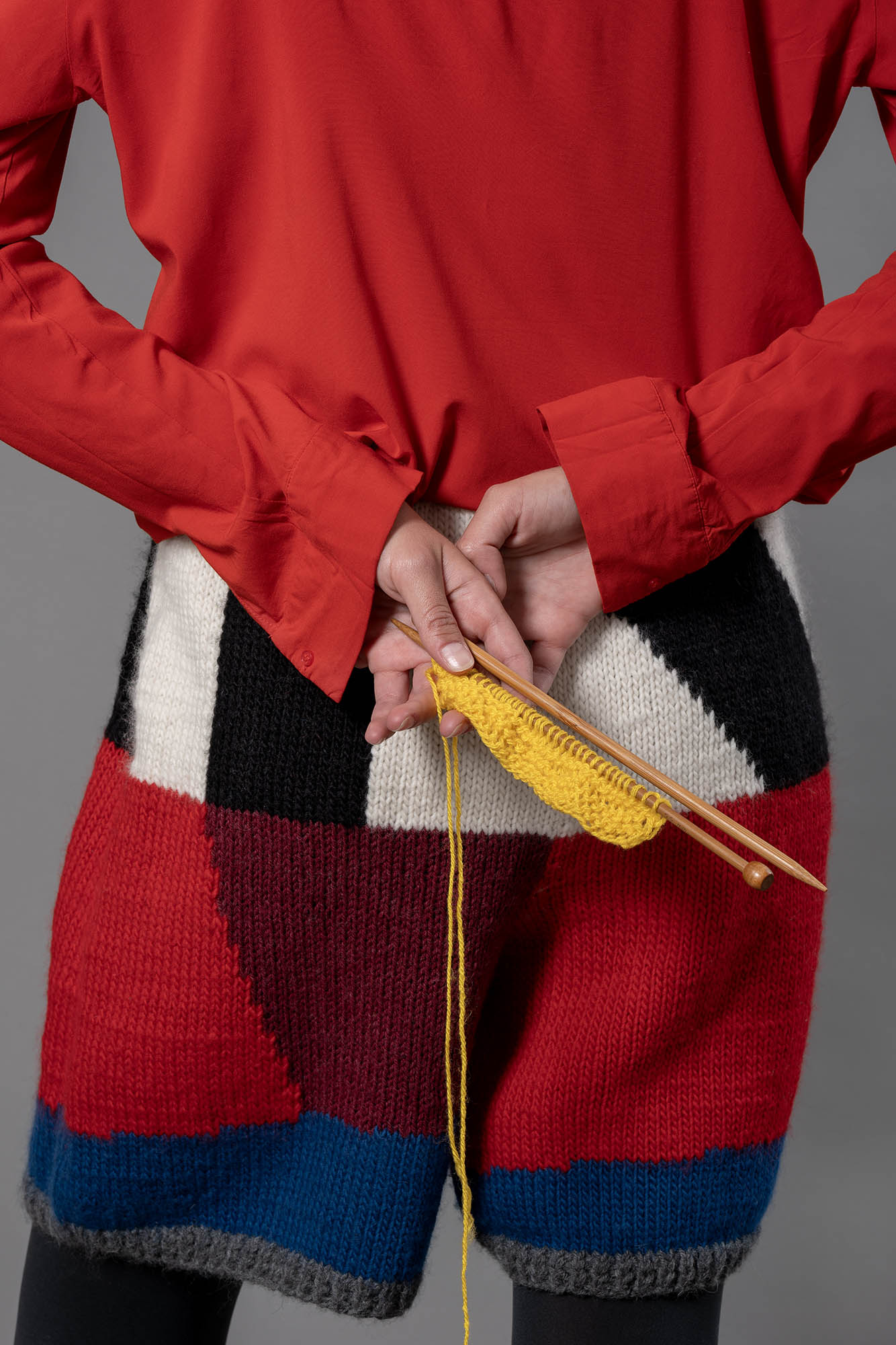 close up of wool bermuda shorts from the back. On the bermuda shorts, black, white, bordeau, red and blue colour block pattern with ribbed grey leg openings