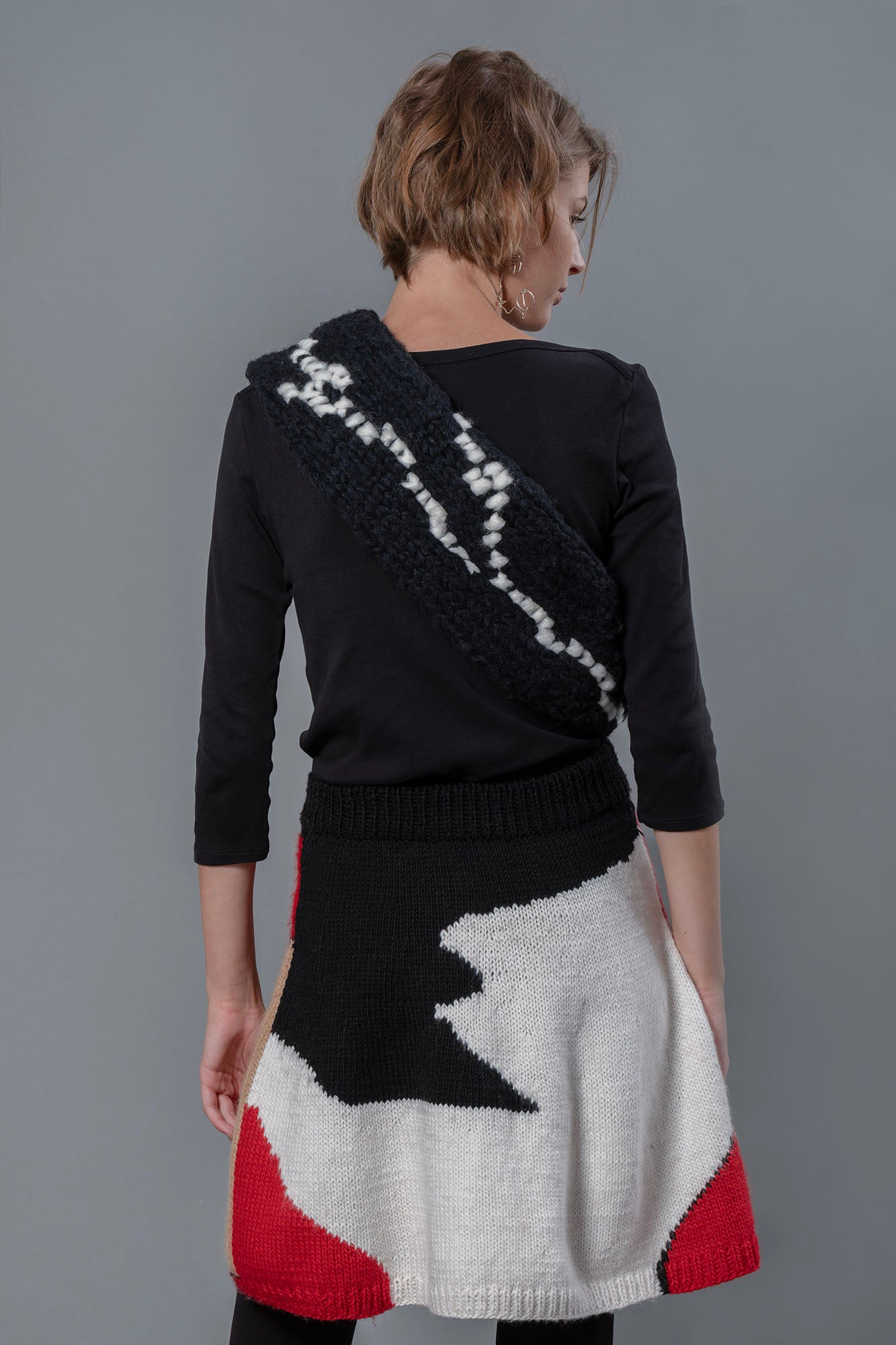 Woman wearing black scarf, black top and wool skirt. The skirt is a mix of mostly white, black and red forming abstract shapes.