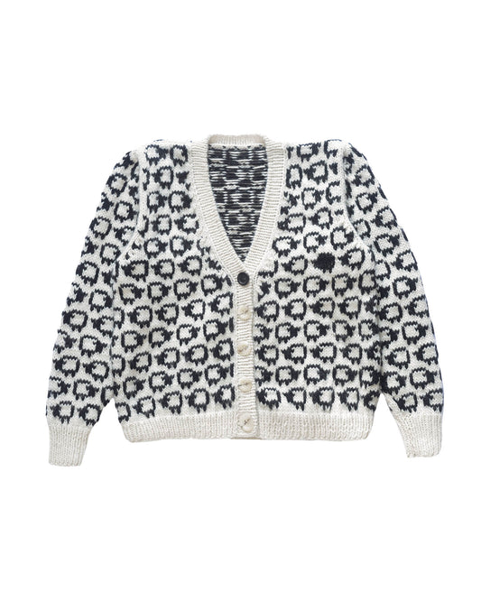 Wool cardigan laid flat on white background. The cardigan has a herd of white sheep all over with a single black sheep on the left side.
