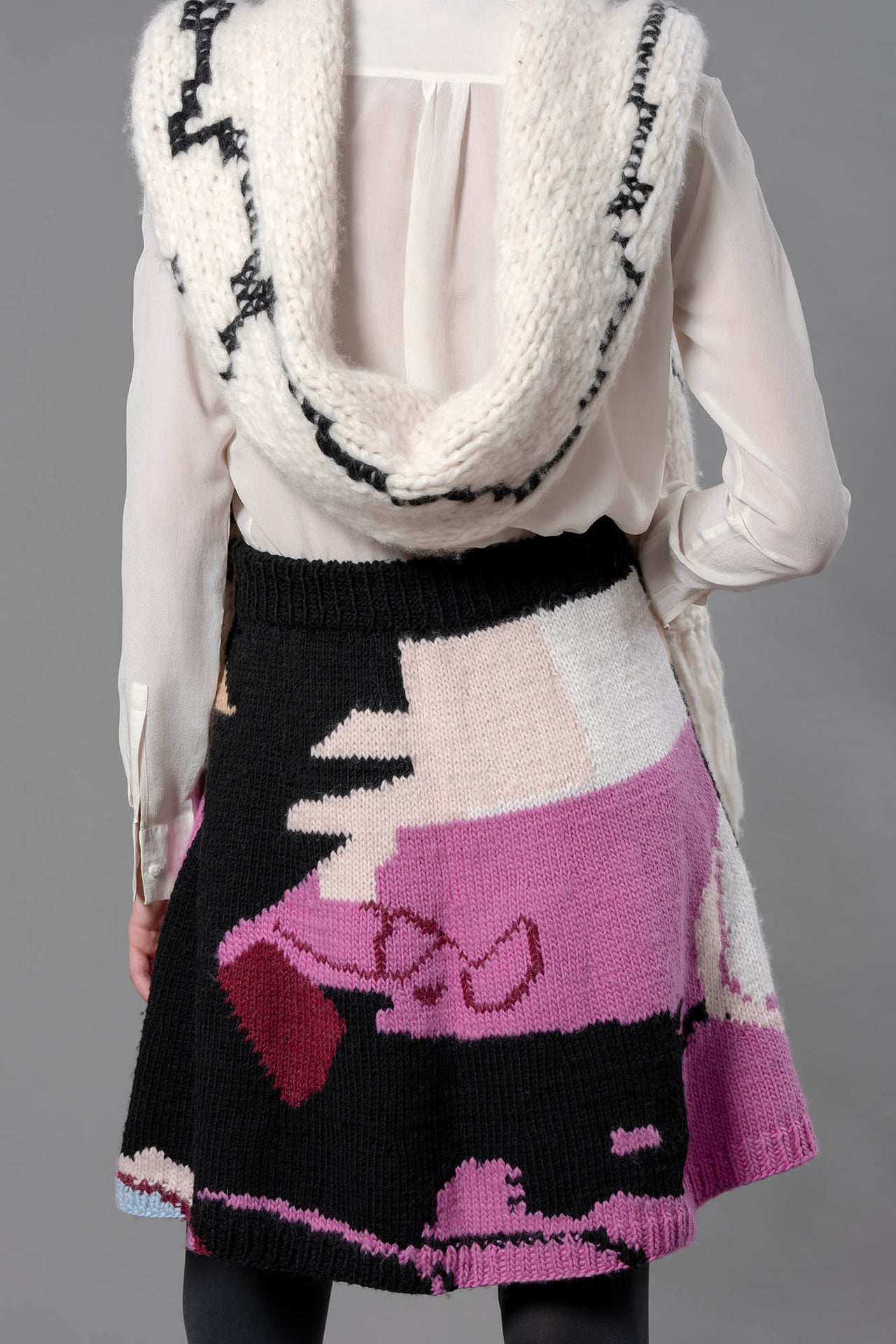 Back of woman wearing wool skirt and black and white wool scarf. The skirt has abstract colour block patterns in fuchsia, black, white, beige and a touch of burgundy.