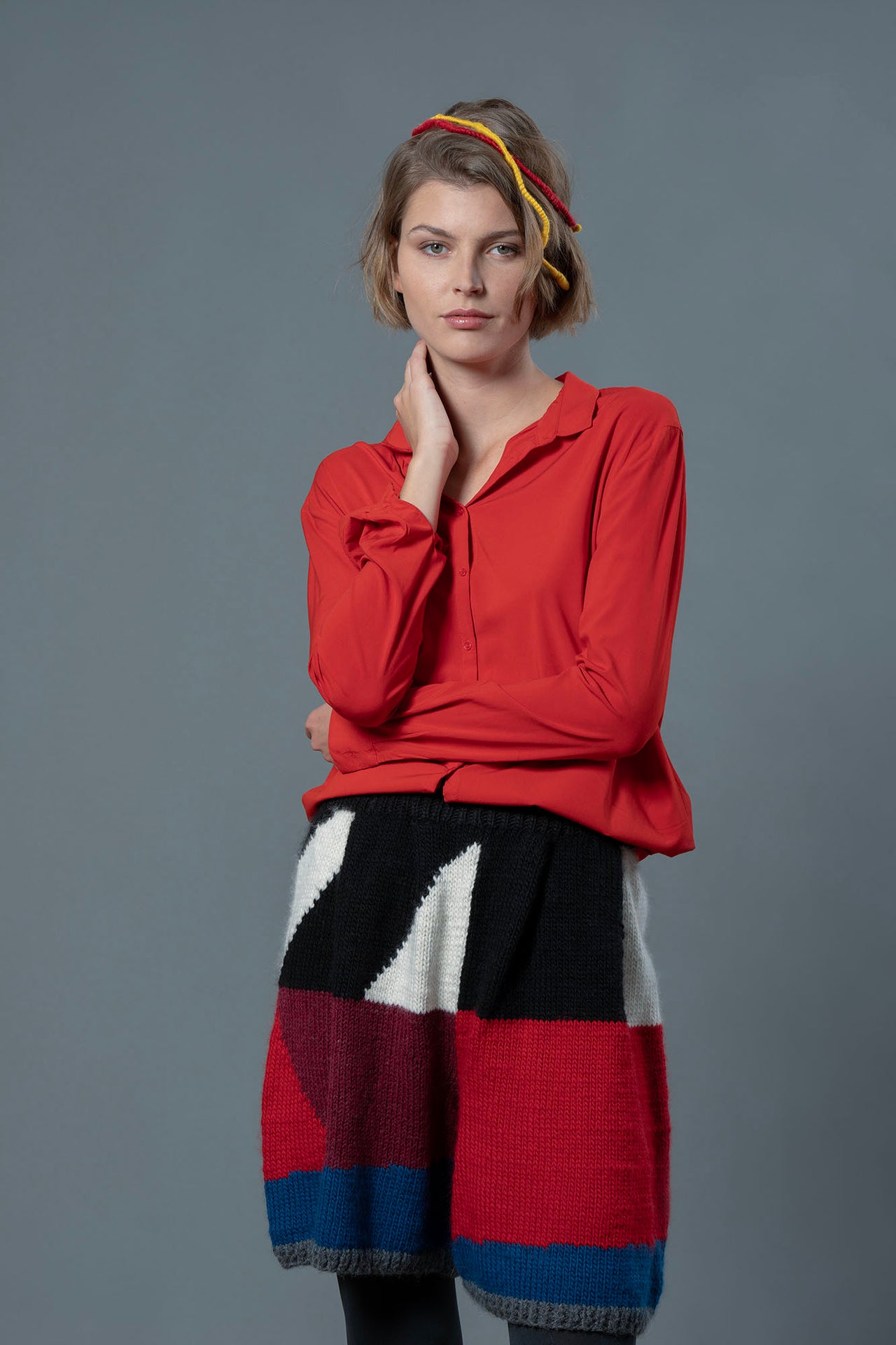 woman wearing red button up shirt and wool bermuda shorts with black, white, bordeau, red and blue colour block patterns. 