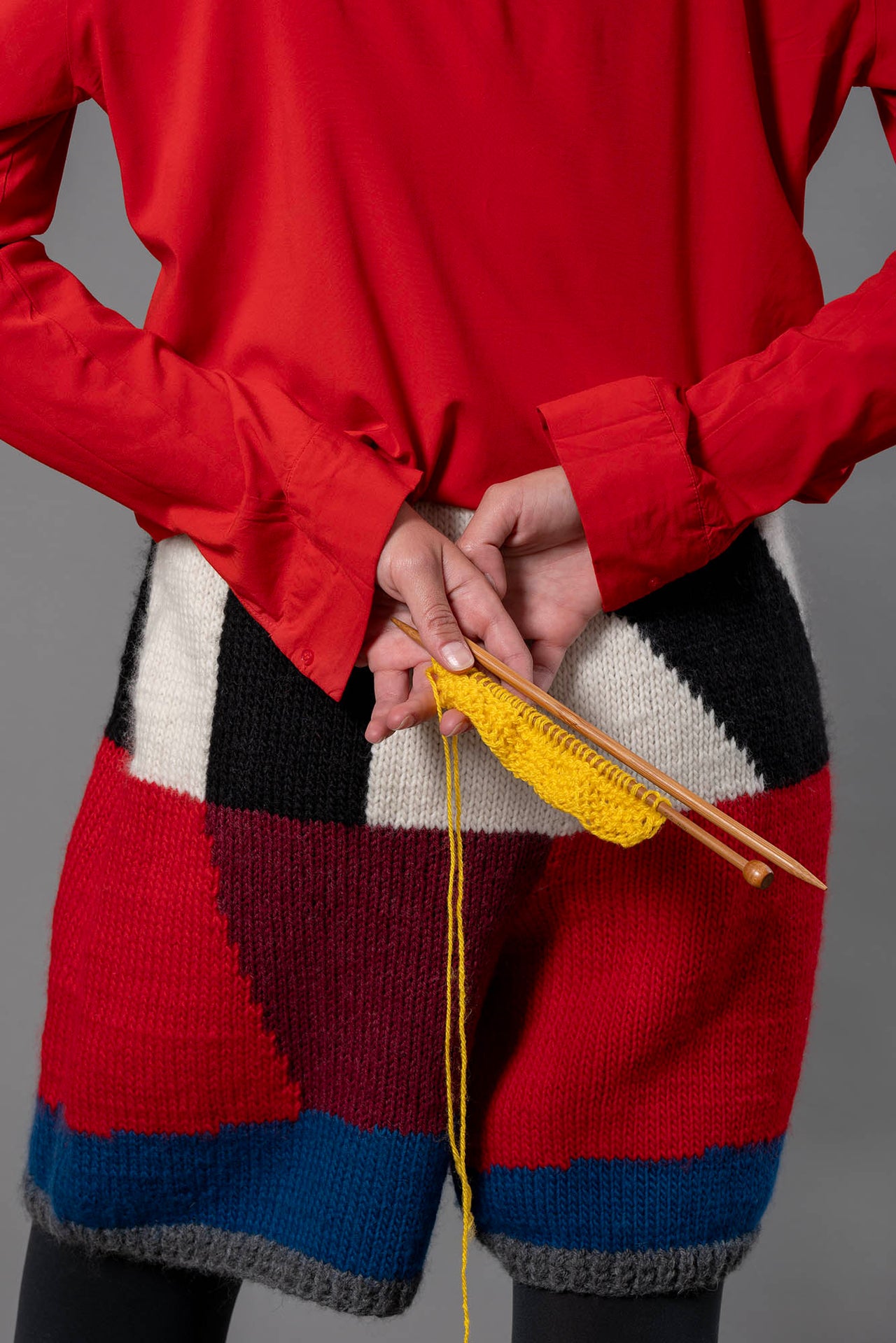 close up of wool bermuda shorts from the back. On the bermuda shorts, black, white, bordeau, red and blue colour block pattern with ribbed grey leg openings 