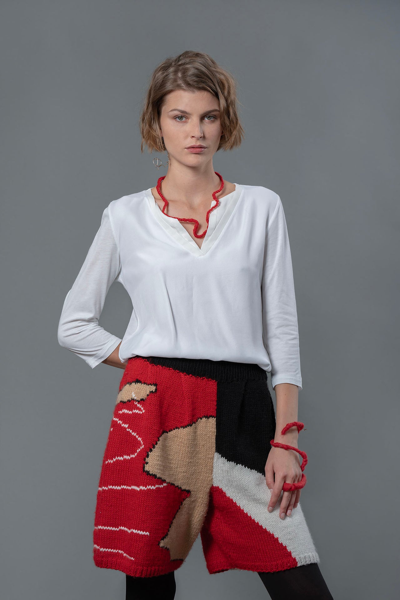 Woman wearing white top and wool bermuda shorts with red, black, white and beige colour block pattern. 