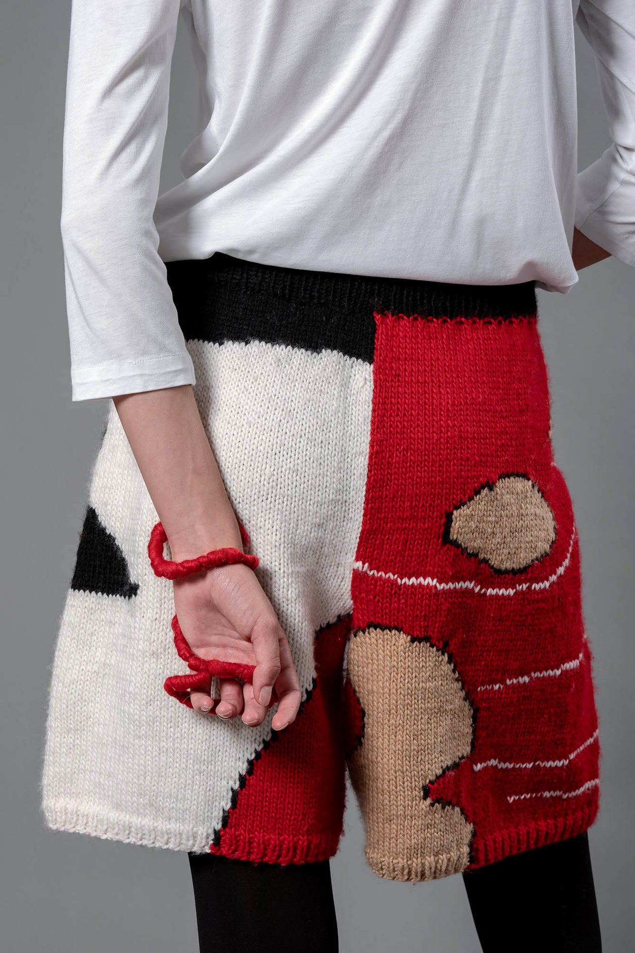 Woman from the back wearing wool bermuda shorts with red, black, white and beige colour block patterns. 