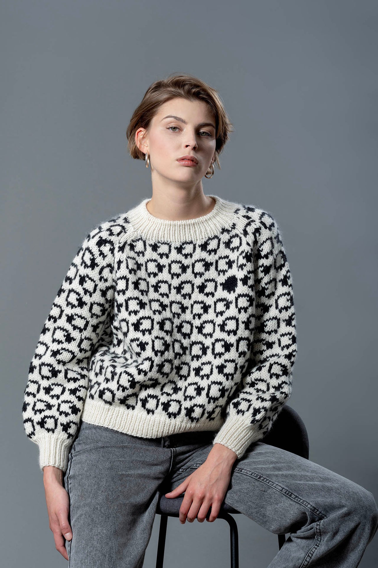 Handmade wool sweater with cropped cut and puffed sleeves. On the sweater is a herd of white sheep going all around, a single black sheep is on the front top left of the sweater. 