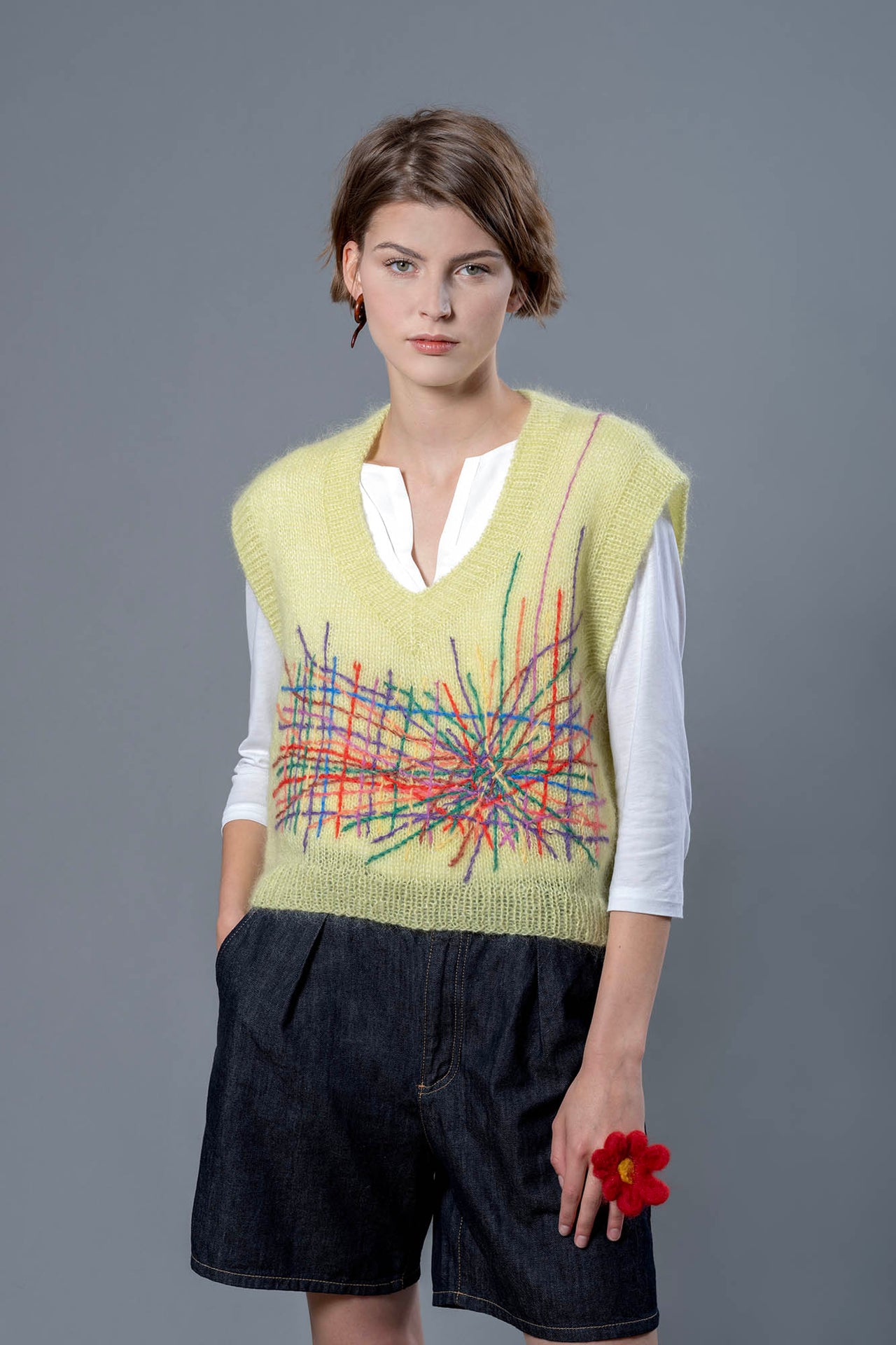 Woman wearing a yellow mohair vest. The vest has a multitude of colourful embroidered lines in its center 