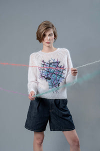 Thumbnail for Woman wearing light pink mohair sweater and holding wool yarns going towards camera. The sweater has colourful embroidered lines forming an abstract shape in the center. 
