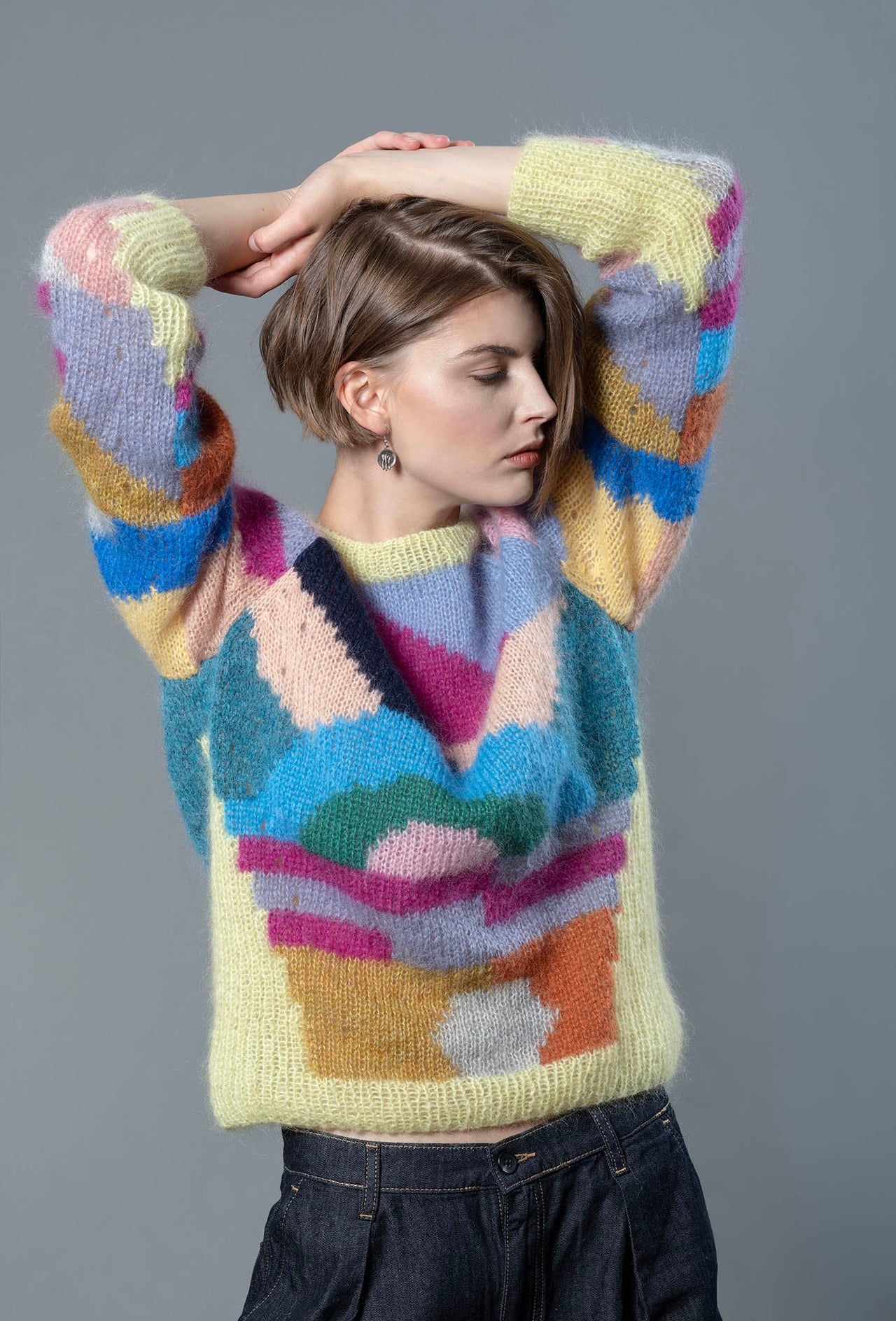 Woman wearing a mohair sweater. The sweater is yellow and is covered with colourful abstract colour block patterns on most of its surface.