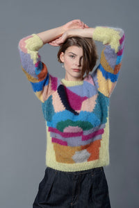 Thumbnail for Woman wearing a mohair sweater. The sweater is yellow and is covered with colourful abstract colour block patterns on most of its surface.