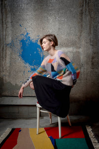 Thumbnail for Woman wearing a mohair sweater sitting on chair. The sweater is beige and is covered with colourful abstract colour block patterns on most of its surface.