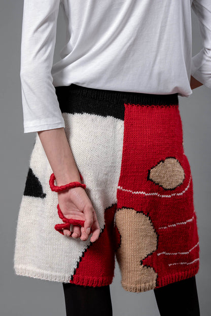 Woman from the back wearing wool bermuda shorts with red, black, white and beige colour block patterns. 