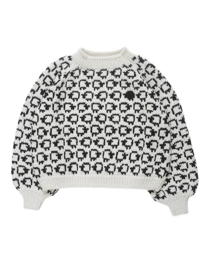 White wool sweater layed flat on white background. On the sweater is a herd of white sheep going left to right all around and a single black sheep on the front. 