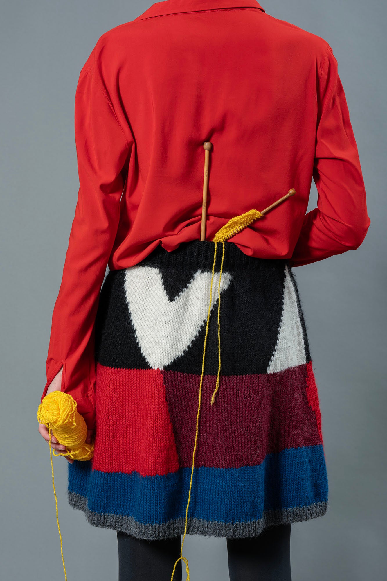Back of woman wearing red top and wool skirt. The skirt has a colour block design made from blue, red, burgundy, black and white colours.  