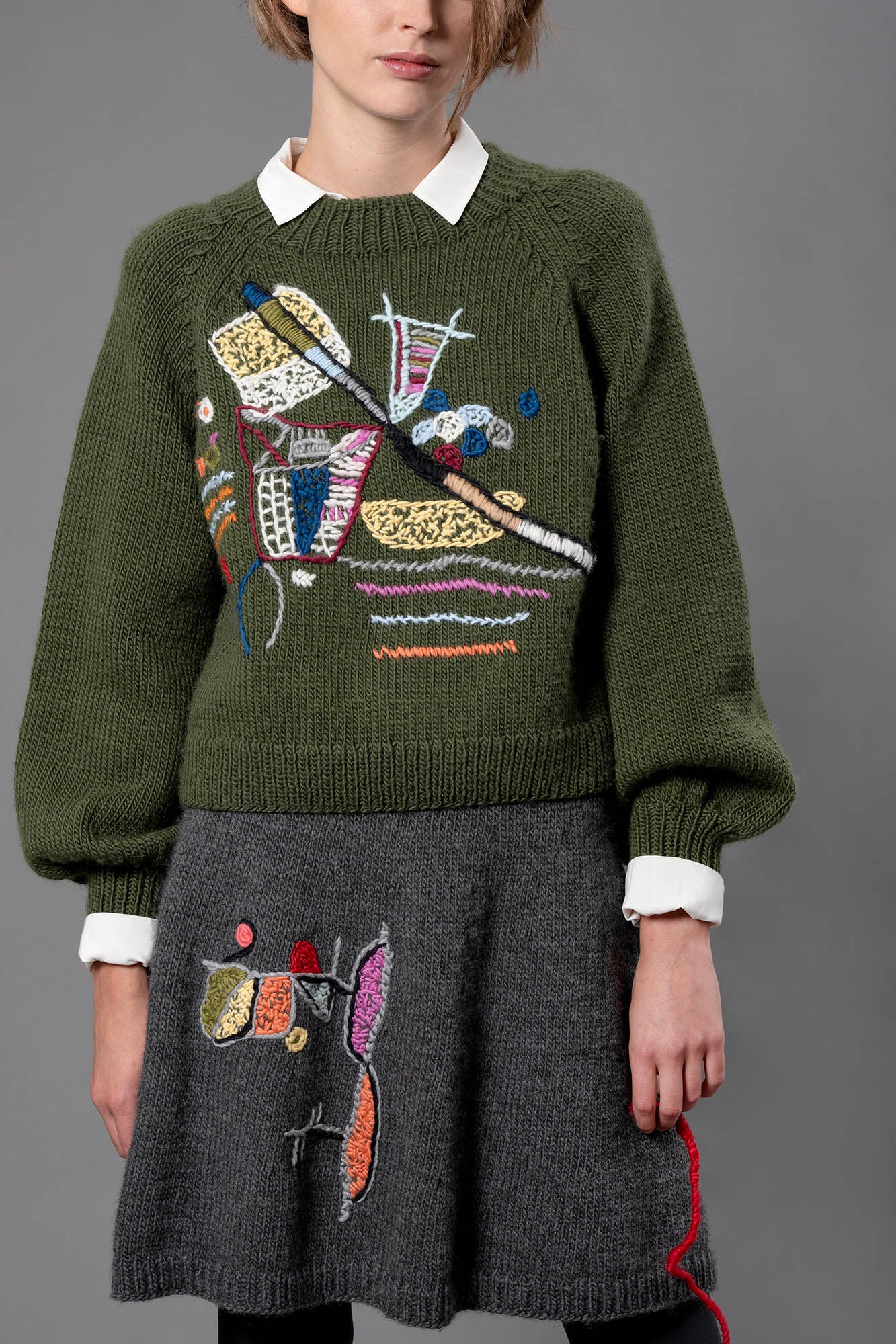 Woman wearing wool sweater and skirt. A grey skirt with a colourful embroidery on the right leg. 