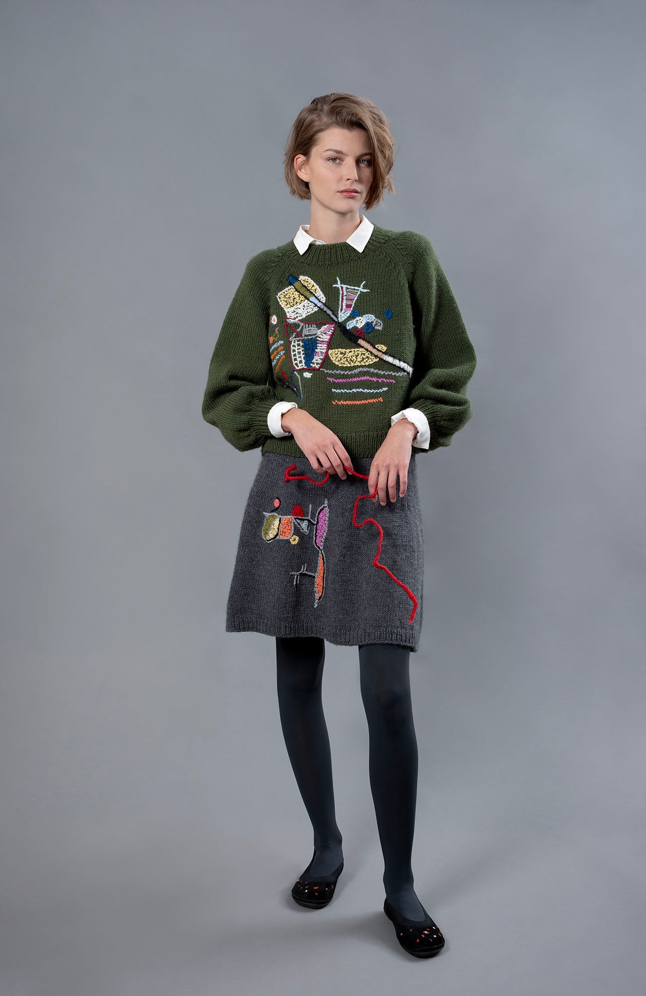 Woman wearing wool sweater and skirt. A grey skirt with a colourful embroidery on the right leg. 