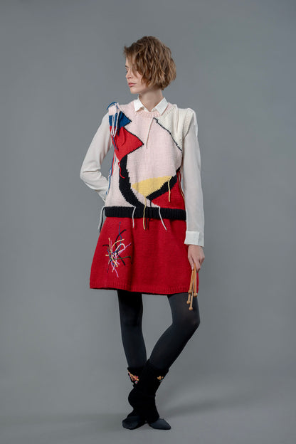 Woman wearing wool vest and red wool skirt. The skirt is knee length and has colourful embroidered lines on the right leg.