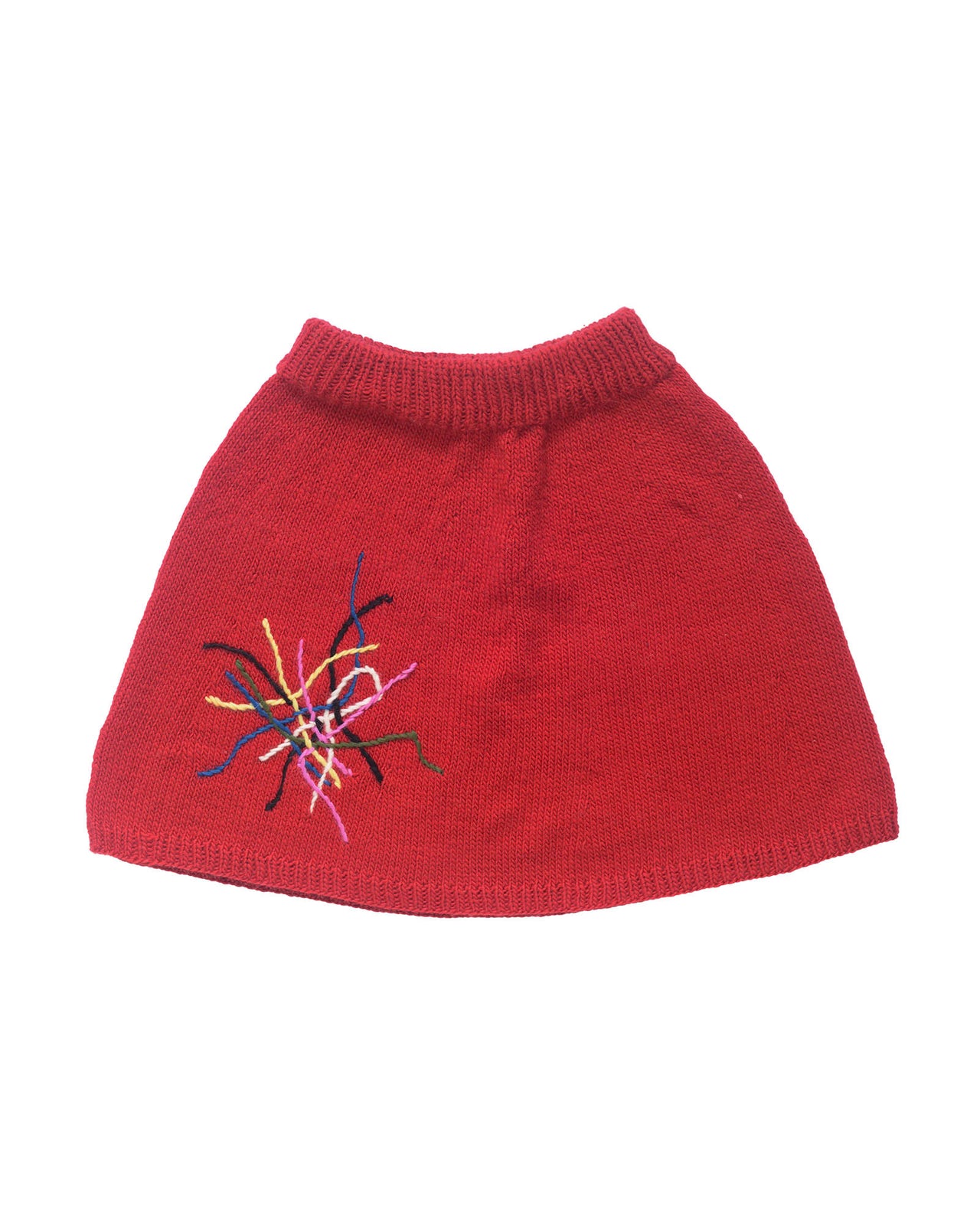 Red wool skirt laid flat on white background. The skirt is adorned with colourful embroidered lines on the right leg. 