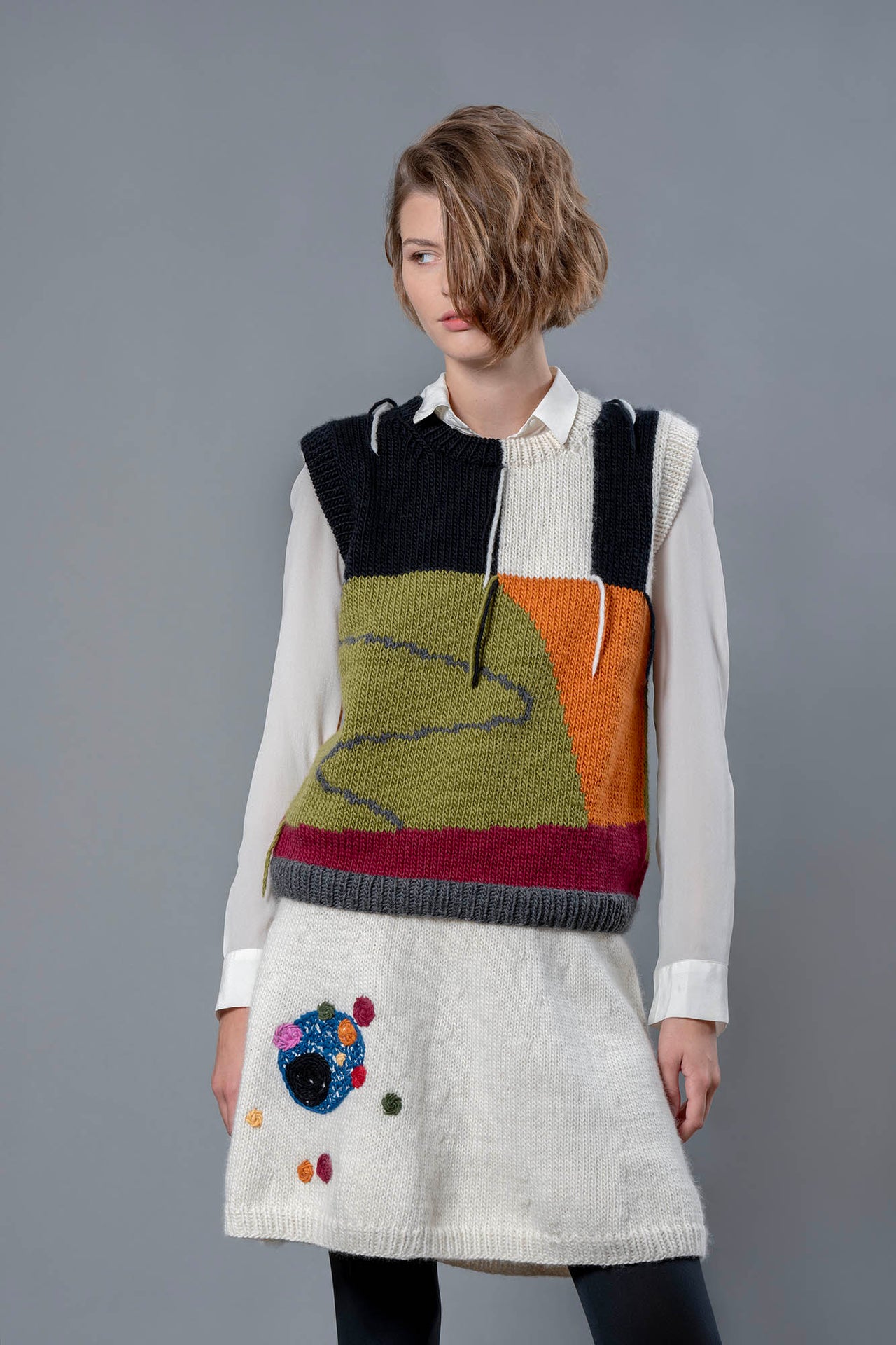 Women wearing wool vest and skirt. Vest has a colour block design of green, orange, black and white, with touches of red. 